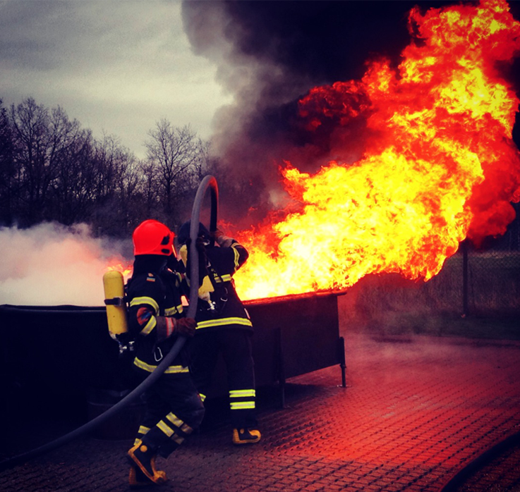 To brandmænd i gang med at slukke en oliekar i brand - Slukkes med svanehals teknikken - Store flammer
