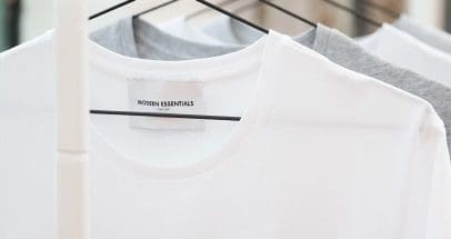 Nærbillede af hvide og grå t-shirts på bøjler. Den forreste t-shirt har mærket "Modern Essentials New York